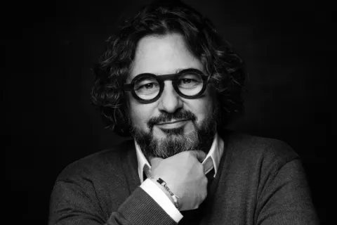 Portrait noir et blanc d’un homme barbu à lunettes, main au menton.