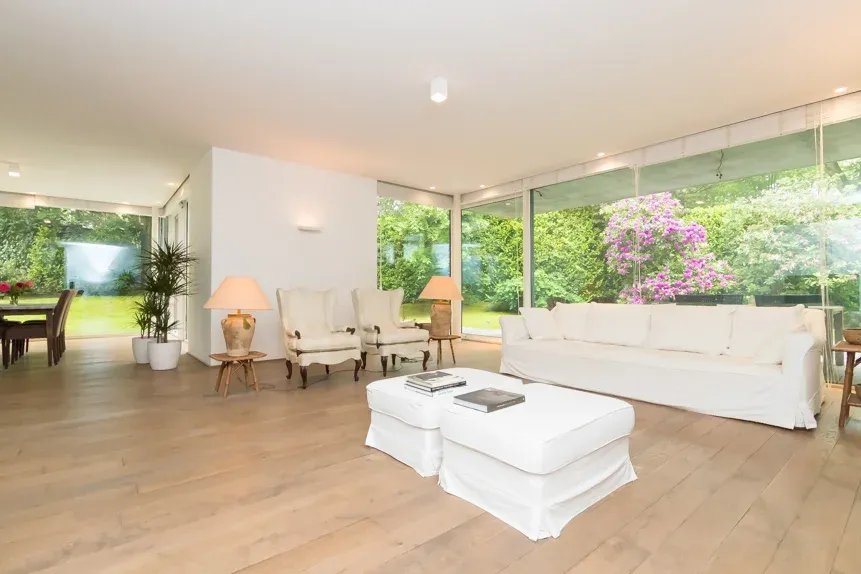 Salon lumineux ouvert sur un jardin, baies vitrées et canapés blancs.
