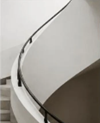 Un escalier courbe en béton clair, avec une main courante noire.