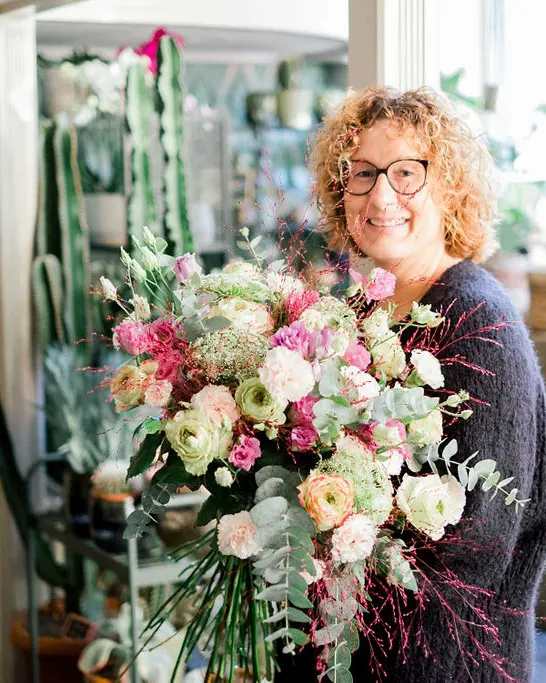 Sophie sourit et compose un bouquet de roses au milieu des fleurs pastel de la boutique