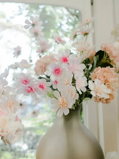 Cosmos roses et œillets pêche dans un grand vase mat, devant une fenêtre