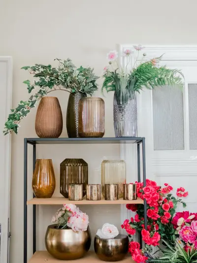 Vases en verre ambré, photophores dorés et cache-pots en laiton sur une étagère