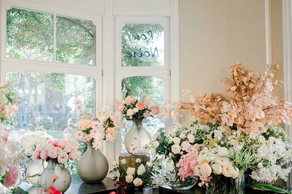 La vitrine de Rose Noire, rue Américaine : de grands vases de roses pastel et des branches fleuries devant les fenêtres