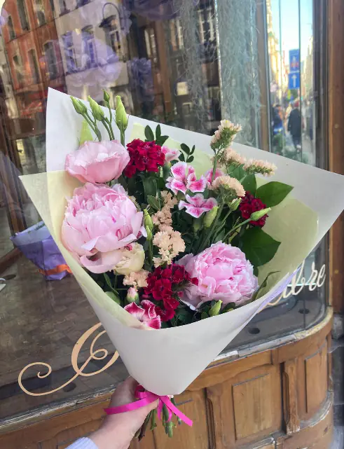 Boeket « Un peu »: roze pioenen, rode anjers en seizoensbloemen in crèmekleurig papier