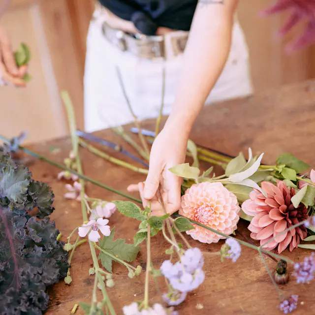 Handen die een boeket met dahlia’s schikken op de houten tafel van het atelier